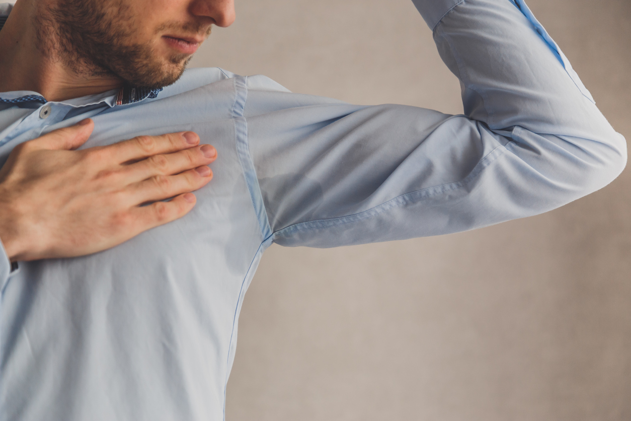 Man with hyperhidrosis sweating very badly under armpit in blue shirt, on grey