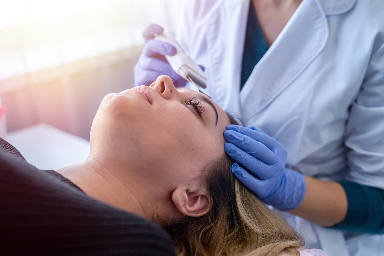 Doctor doing procedure of ultrasonic cleaning of face patient in beauty salon. Professional skin care