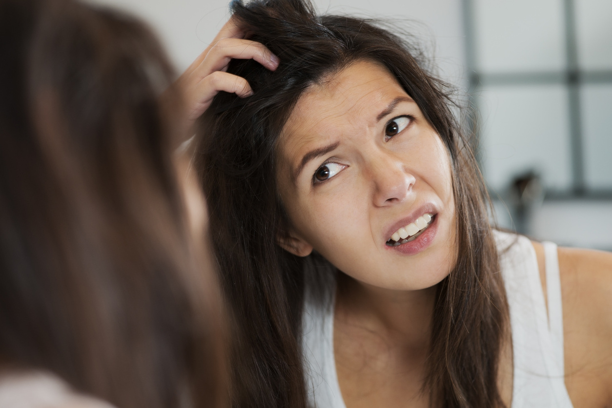 Woman having a bad hair day grimacing in disgust as she looks in the mirror and runs her hands through her hair